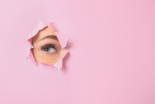 Eye Of Beautiful Young Woman Visible Through Hole In Pink Teared Paper