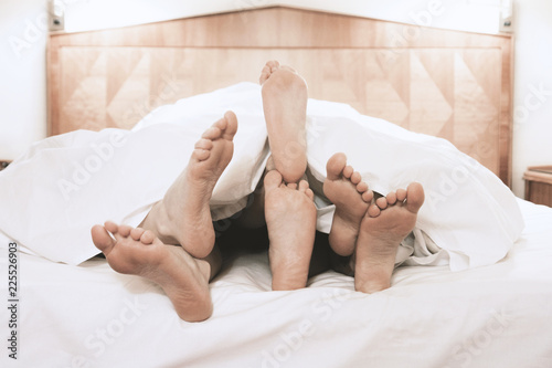 Fotomural three pairs of feet lying together under bed cover in bedroom, threesome group s
