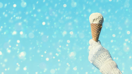 Female hand in knitted gloves with ice cream in a waffle horn on the blured background. Concept. 