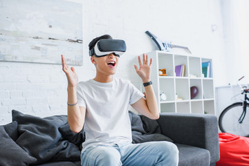 Wall Mural - happy young asian man sitting on couch and using virtual reality headset at home