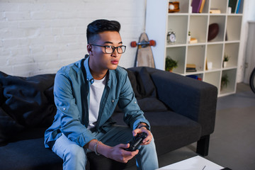 Wall Mural - focused young asian man playing video game with joystick at home