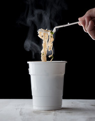 Wall Mural - Hand holding plastic fork of hot instant noodles with steam and smoke in white cup