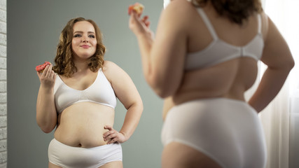 Wall Mural - Confident fat lady in underwear happy with mirror reflection, eating sweet donut