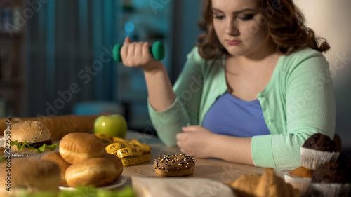 Cuadros en Lienzo Overweight lady exercising and sadly looking at junk food, obesity problem