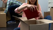 Young woman unpacking photo album from box, couple moving to new apartment