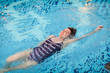 © Aleksandra - Beautiful adult woman in striped swimsuit swimming in blue pool on her back at resort. Sport activity health concept.