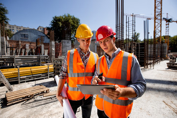 architect and structural engineer dressed in orange work vests and helmets discuss a building projec