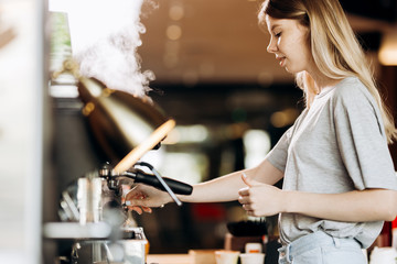 A good looking slim blonde with long hair,dressed in casual outfit,is cooking coffee in a modern coffee shop. Process of making coffee is shown.