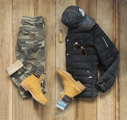 Wall Mural - Fashionable concept, men’s clothes with yellow boot, coat, military pants, watch, key chain and sunglasses on wooden background. pack shots, top view