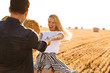 Photo of lovely couple man and woman laughing while walking through golden field with bunch of haystacks, during sunny day