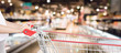 Woman hand hold empty red shopping cart with abstract blur supermarket discount store aisle interior defocused background with bokeh light