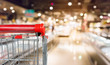 Empty red shopping cart with abstract blur supermarket discount store aisle and product shelves interior defocused background