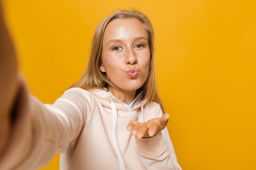 Wall Mural - Photo of blond woman 16-18 with dental braces smiling and taking selfie, isolated over yellow background