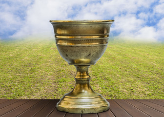 Wall Mural - Old chalice on wooden table with clouds background