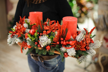 Woman holding a decorative table Christmas composition made of fir tree, red candles, flowers and balls on wooden board