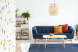 Lamp above wooden table in front of blue sofa with cushions in colorful living room interior. Real photo