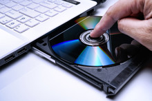 DVD Disk On The White Laptop DVD ROM Tray With A Man Hand. A Piracy Conceptual Image Of Burning Data Into DVD Disk