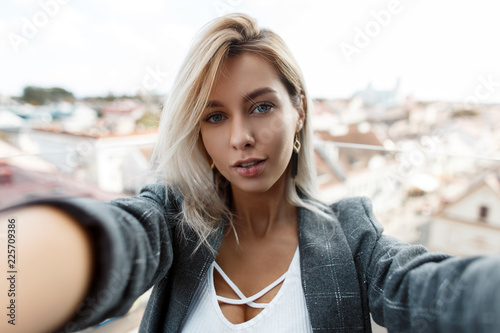 Fotografía Beautiful stylish young woman in a vintage fashion coat is traveling and photographing on the roof of the city