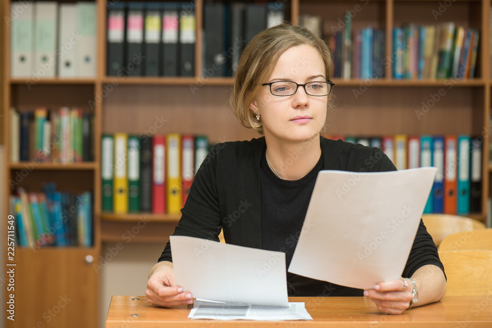 Girl student or teacher smiles sits at her desk dressed in glasses and ...