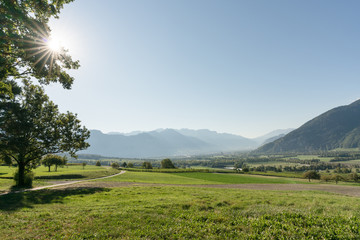 Canvas Print - panorama countryside view with sun shining and fields and forest and mountains in early autumn