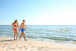 Happy young couple in beachwear walking together on seashore