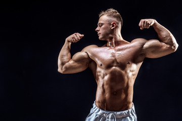 Handsome strong bodybuilder posing in studio on black background