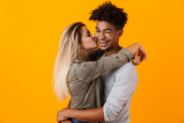 Wall Mural - Cute young loving couple posing isolated over yellow background hugging.