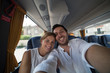 © photomaticstudio - Backpackers traveling around the world on the bus. Young handsome man with his girlfriend on traditional bus taking selfie on smartphone.