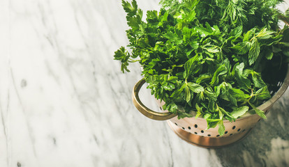 Bunch of fresh green garden herbs in brass colander over marble kitchen table background, top view, copy space, horizontal composition