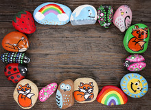 Border Of Colorful Cartoon Hand Painted Animal Rocks On Wood Background