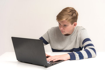 Portrait of a teen boy on a white background at the table with a laptop.