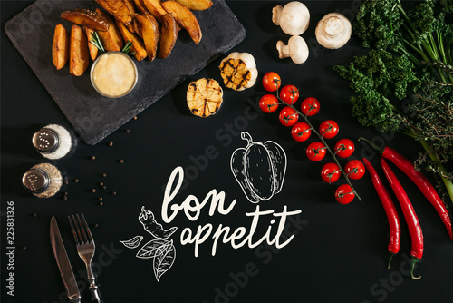 Plakaty do jadalni top-view-of-tasty-baked-potatoes-with-sauce-spices-and-vegetables-on-black-with-bon-appetit-lettering