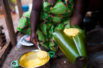 detail of traditional african corn foufou on plantain leaf held by black woman cooking in humble home kitchen