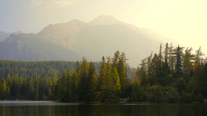 Wall Mural - Peaceful mountain scene with calm lake, colorful trees and high peaks in a golden warm light. Scenic view of Strbske Pleso, High Tatras National Park, Slovakia.