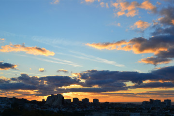 Wall Mural - Cityscape in the early morning: the blue sky and clouds are colored yellow-orange by the rising sun over the sleeping city background