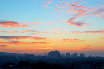 Wall Mural - Cityscape in the early morning: pink and orange clouds on a blue sky at dawn just before sunrise over the sleeping city background