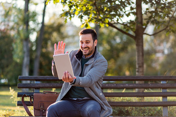 Businessman make video call using digital tablet while sitting on a bench in a park