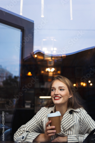 Fotografía Young beautiful smiling woman in striped trench coat holding cup to go in hand h