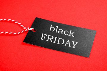 Wall Mural - Black friday sale concept. Fourth Thursday of November, beginning of Christmas shopping season since 1952. Black tag with white text on bright red background. Copy space, close up, top view, flat lay.