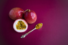 Whole Ripe Passion Fruits, Cut Half, Pulp In A Silver Spoon On Dark Red (burgundy) Background.