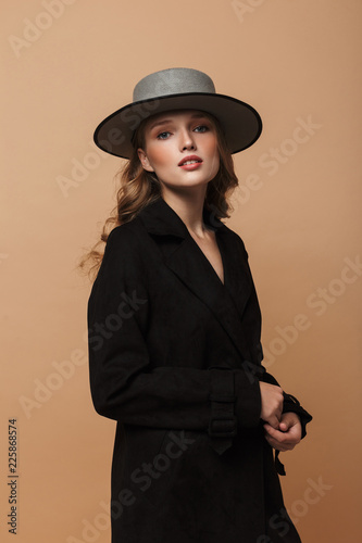 Fotografia Young attractive woman with wavy hair in black coat and hat thoughtfully looking