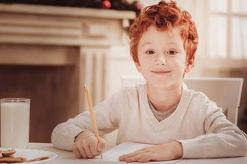 Wall Mural - Spending time with pleasure. Close up of diligent little boy looking at you while sitting at the table and drawing