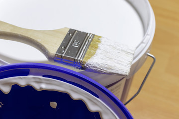 Wall Mural - A brush lying on the edge of paint bucket with white paint.