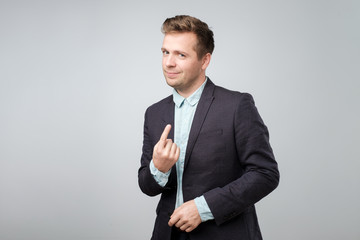 Sticker - Studio portrait of playful mature adult showing come here gesture with index finger and smiling over gray background.