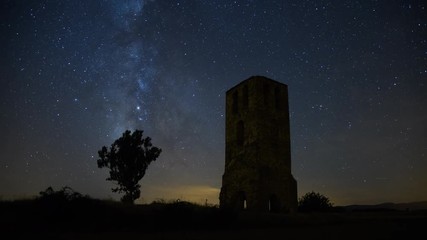 Wall Mural - the milky way moving across the night sky and an ancient castle tower lit by the moonrise in a clear