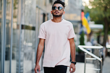 Stylish indian beard man at sunglasses and pink t-shirt. India model posed outdoor at streets of city.