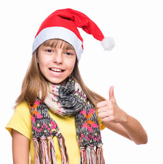 Wall Mural - Half-length portrait of caucasian girl wearing Santa Claus hat. Schoolgirl looking at camera and making thumb up gesture. Holiday Christmas concept - happy cute child isolated on white background.