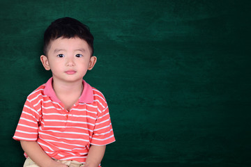 Happy Asian kid smiling on empty green chalkboard with copy space for add text or word, education and back to school concept.