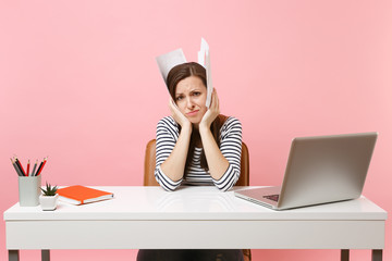 Wall Mural - Tired upset woman hold paper documents near head lean on hands work on project while sitting at office with laptop isolated on pastel pink background. Achievement business career concept. Copy space.