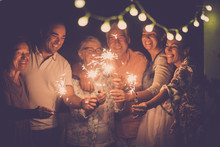 Group Of Caucasian People Friends With Different Ages Celebrate Together A Birthday Or New Year Eve By Night Outdoor At Home. Lights And Sparkles  With Cheerful Women And Men Having Fun In Friendship